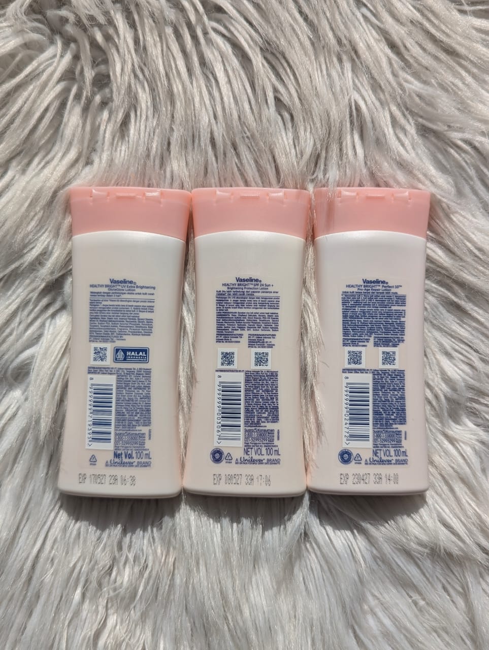 Three baby lotion bottles with pink caps on a fluffy white surface